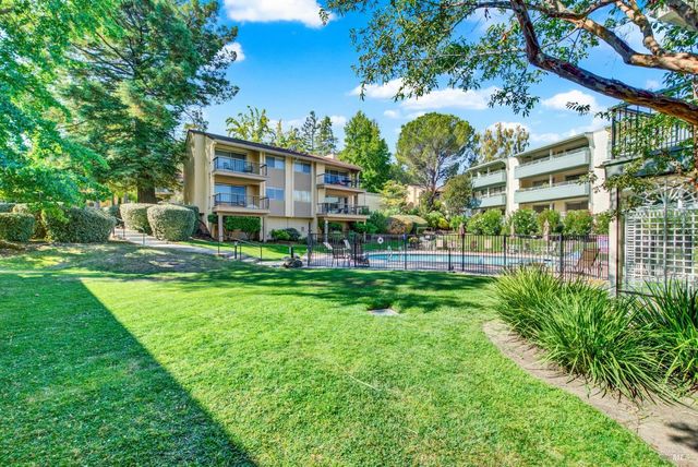 a view of a building in front of a big yard with potted plants and large trees