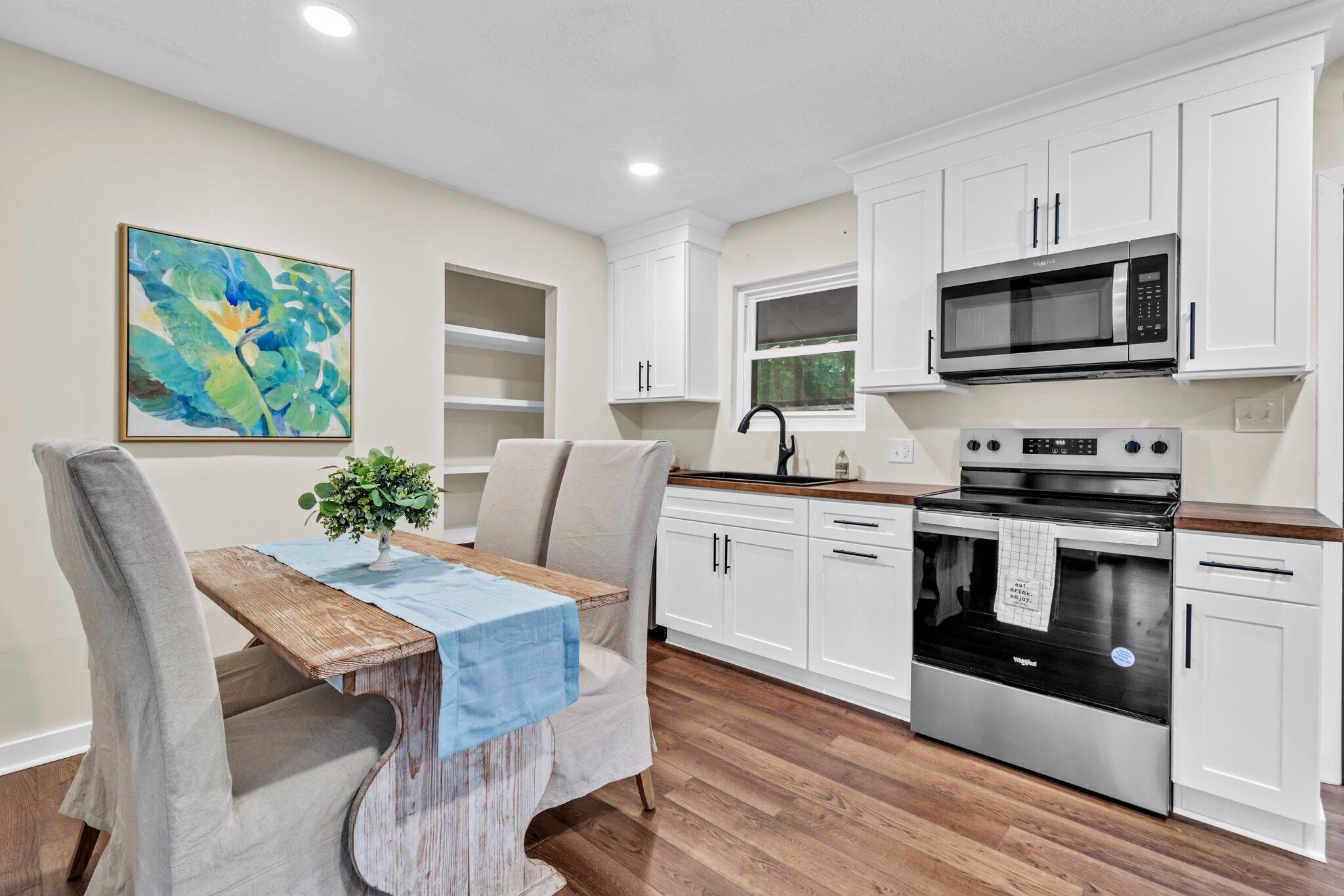 a white kitchen with stainless steel appliances granite countertop a stove top oven a sink a dining table and chairs