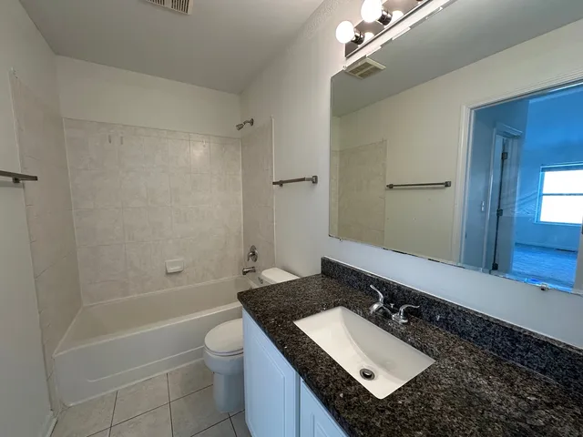 a bathroom with a granite countertop sink a toilet a mirror and shower
