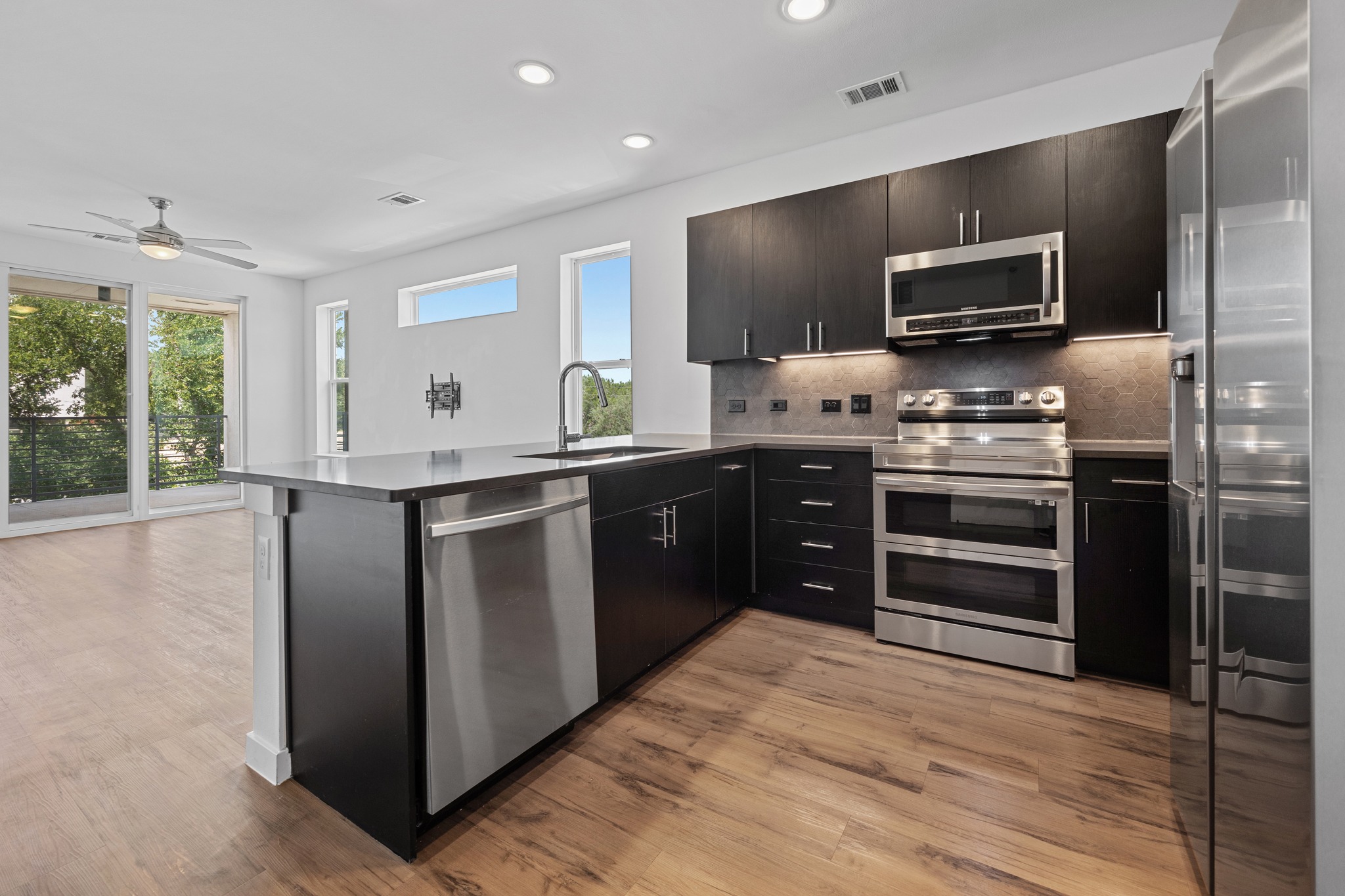 4801 Springdale Road, Unit 2301 Austin, TX 78723 - Photo 5 of 36 A contemporary kitchen space boasts sleek, dark cabinetry and durable wood flooring, complementing a sliding glass door to a private outdoor space.