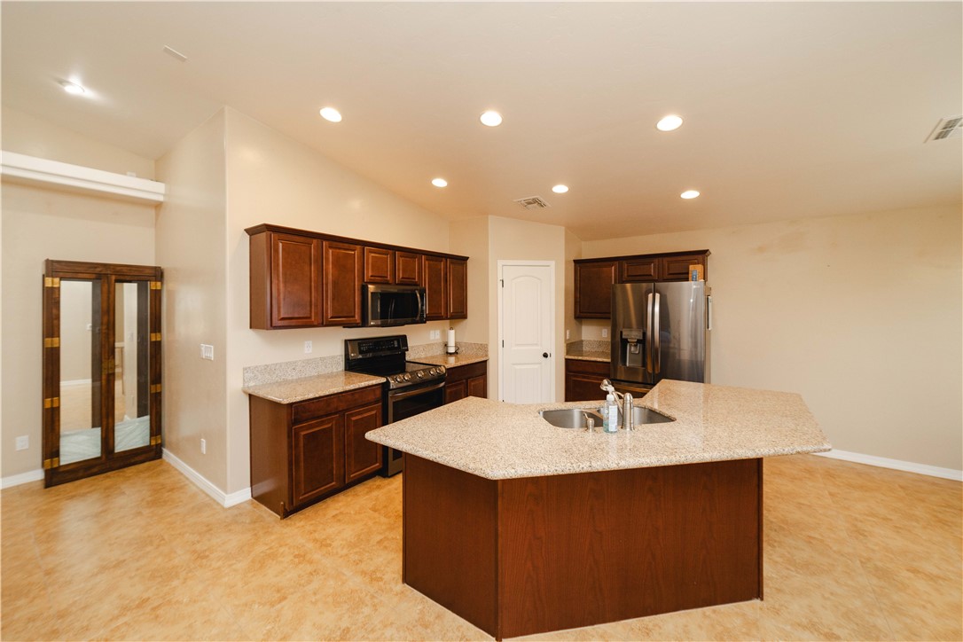 3379 Motherload Road Kingman, AZ 86401 - Photo 16 of 67 Kitchen with appliances with stainless steel finishes, light stone countertops, a kitchen island with sink, recessed lighting, and dark brown cabinets