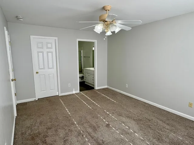 an empty room with a chandelier fan and kitchen view