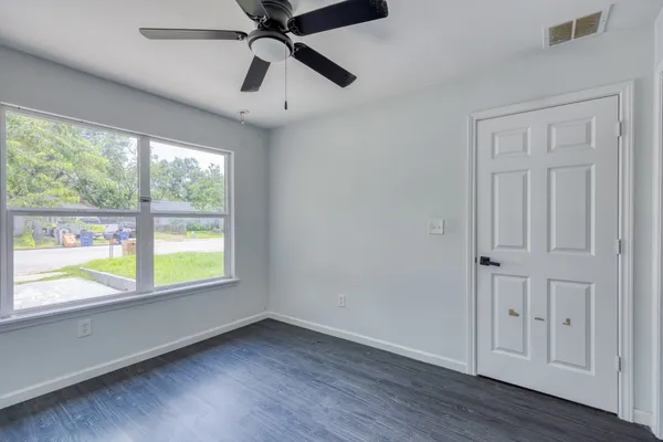 an empty room with wooden floor fan and windows