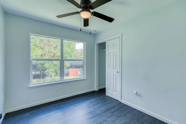 an empty room with wooden floor ceiling fan and windows
