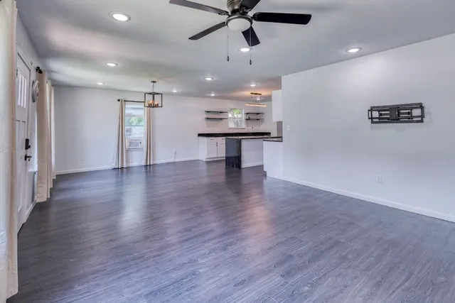 a view of an empty room with wooden floor and a ceiling fan