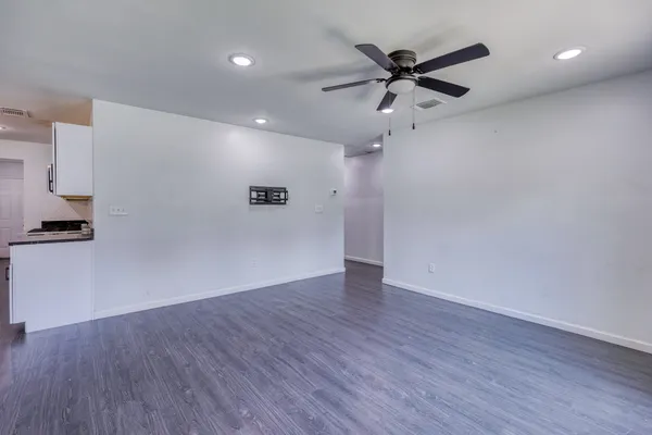 a view of an empty room with wooden floor and a ceiling fan