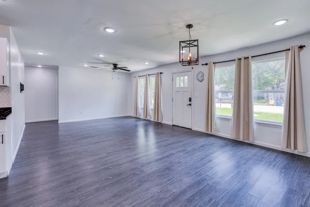 a view of an empty room with wooden floor kitchen view and a window