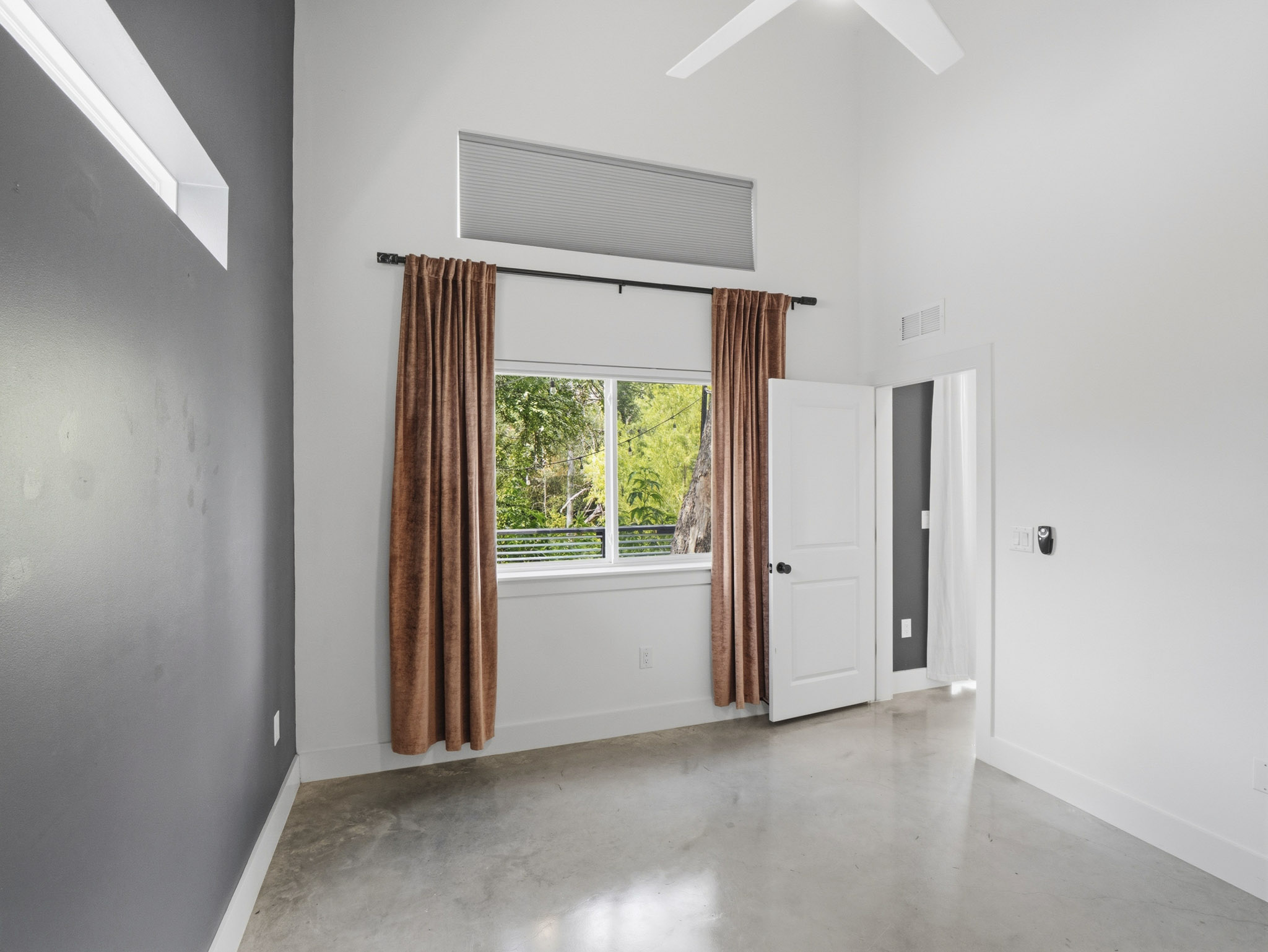 5005 Lott Avenue, Unit 2 Austin, TX 78721 - Photo 12 of 25 A well-lit bedroom features high ceilings, a wide window with views of lush greenery, and smooth concrete flooring.