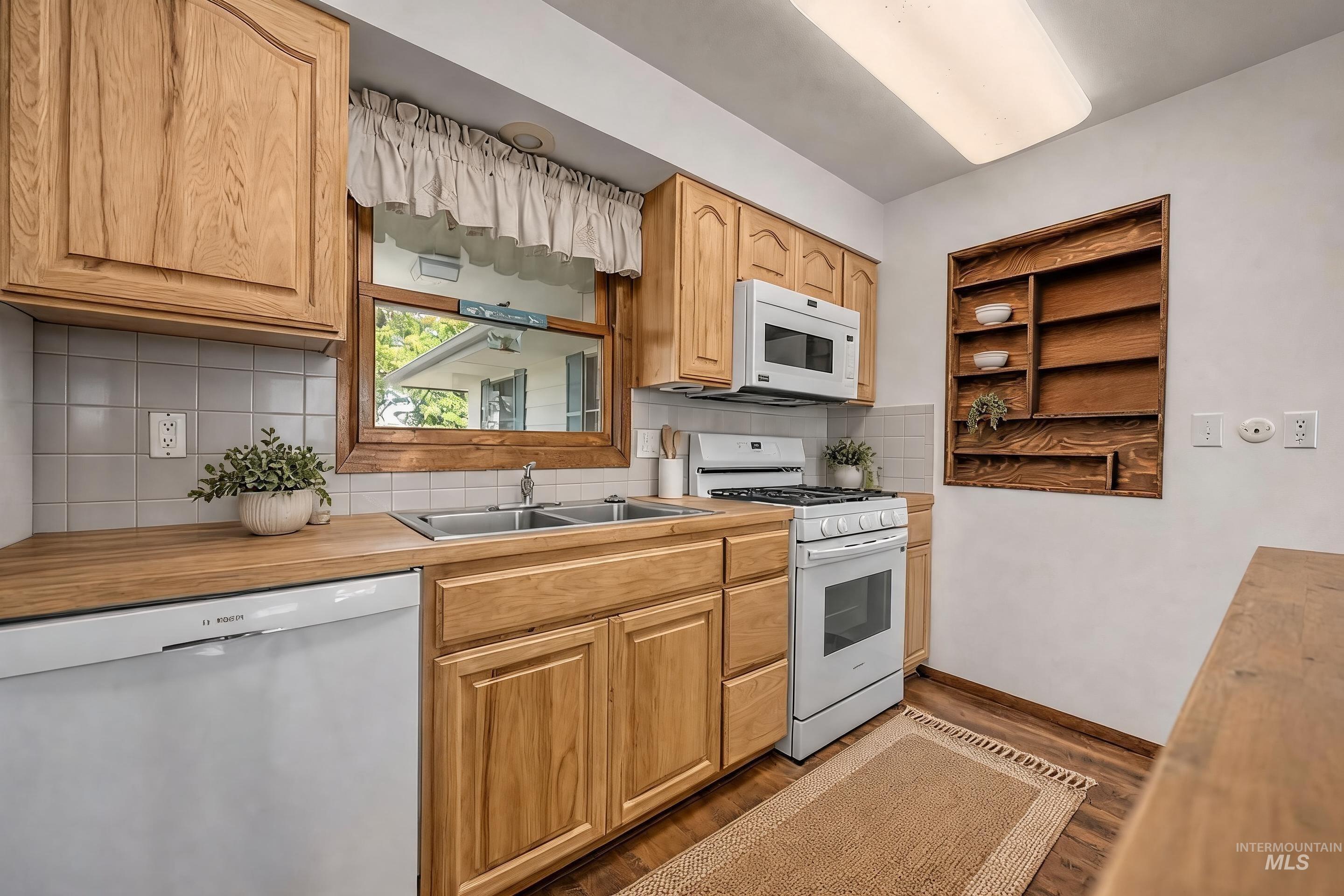 1493 Cove Road Weiser, ID 83672 - Photo 22 of 50 Kitchen featuring wood-finish cabinetry, solid surface countertops, a double basin stainless steel sink, tile backsplash, and wood-finish flooring