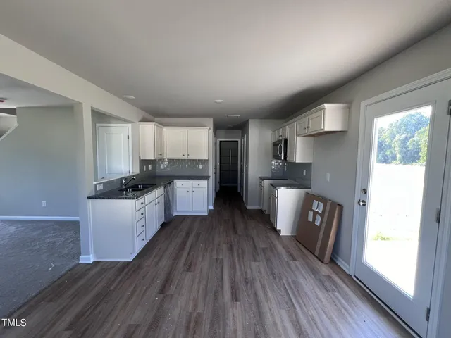 a kitchen with granite countertop a refrigerator a sink dishwasher a stove and white countertops with wooden floor