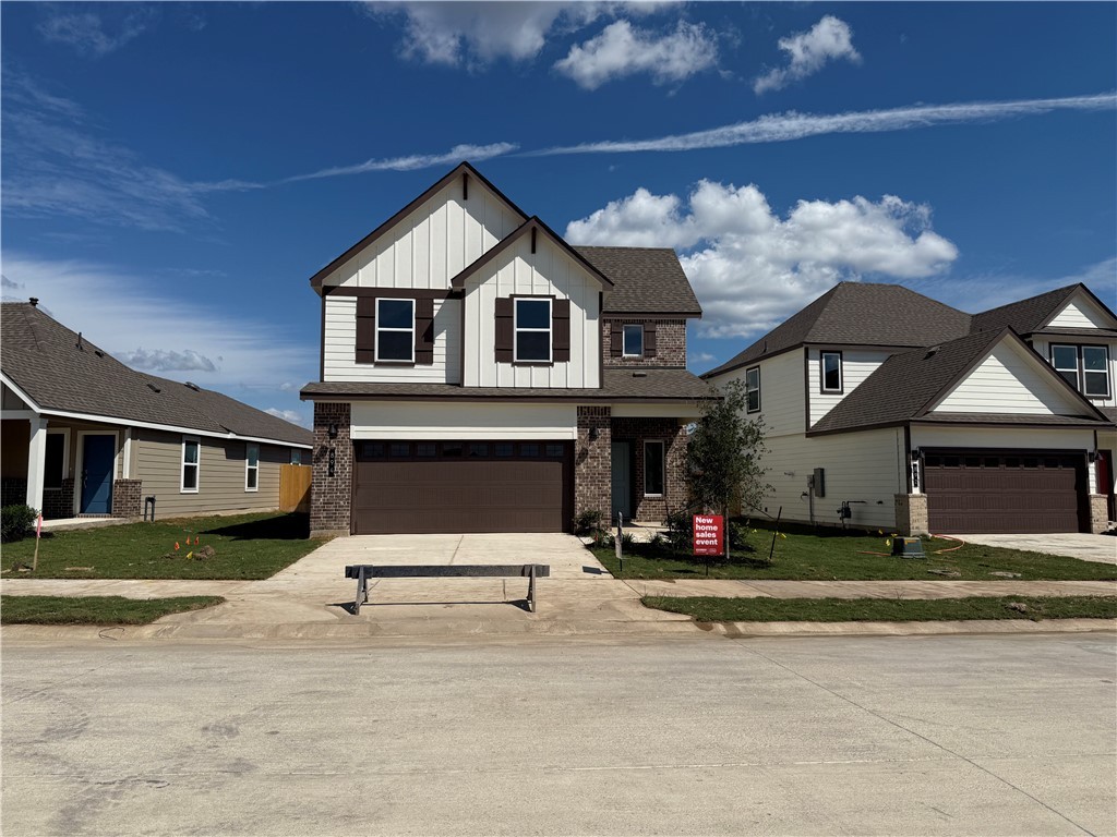 View of front of property with board and batten siding, driveway, brick siding, a front yard, and an attached garage