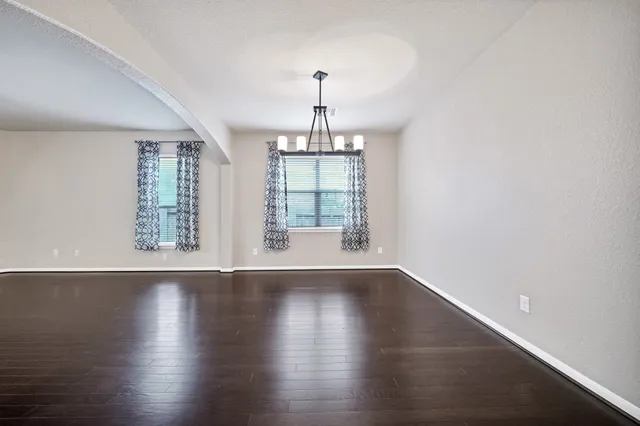 an empty room with wooden floor chandelier and windows