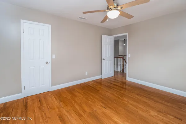 a view of an empty room with wooden floor and a ceiling fan