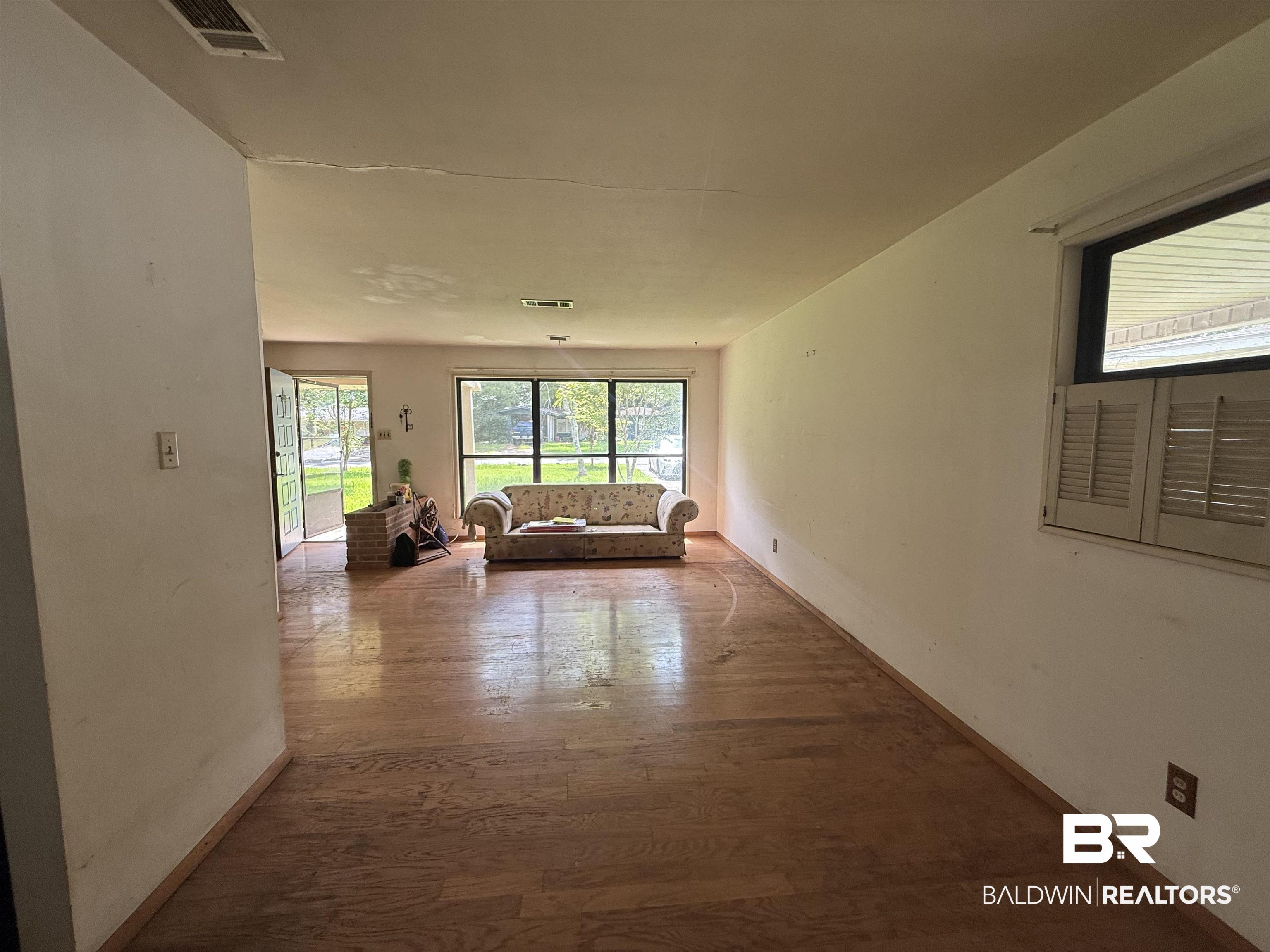 711 Wilshire Road Mobile, AL 36609 - Photo 3 of 11 Spacious living area featuring wood-finish flooring, a large picture window, and a brick hearth