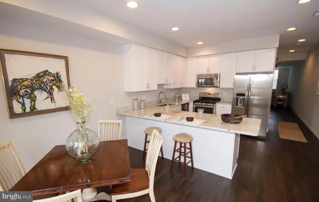 a kitchen with kitchen island a stove a refrigerator a sink a dining table and chairs with wooden floor