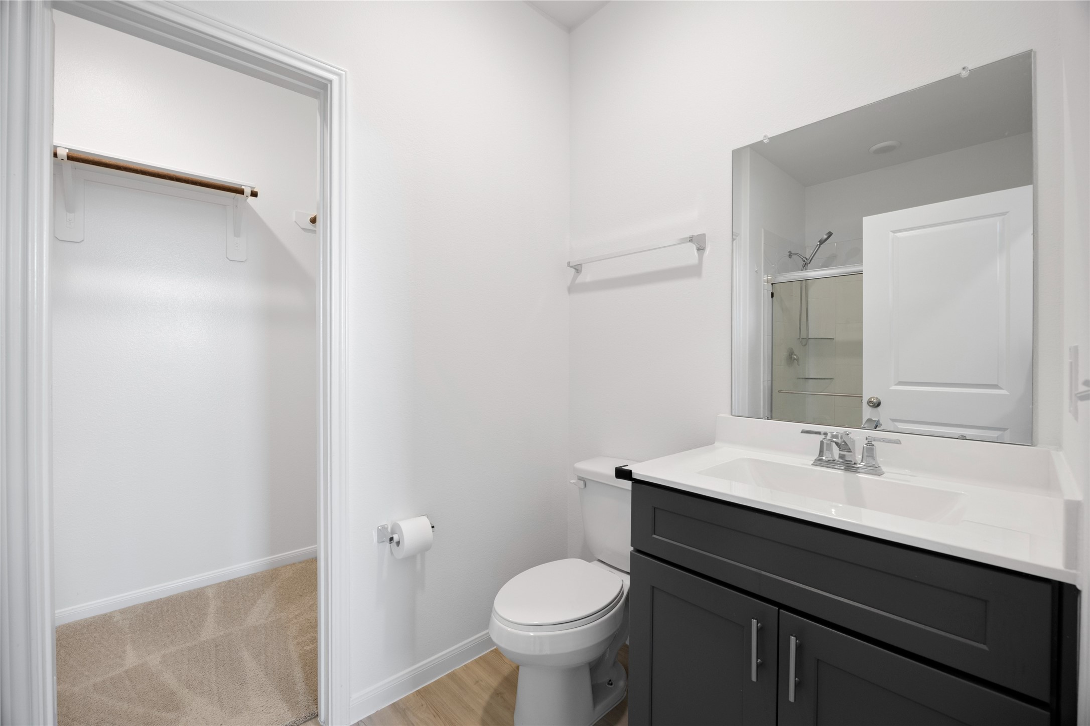 17907 Grain Auger Road Hockley, TX 77447 - Photo 21 of 24 modern bathroom with a sleek vanity featuring a large mirror. It includes a toilet and a shower area with a glass door. Adjacent is a walk-in closet with ample storage space. The room is bright and clean with a neutral color palette.