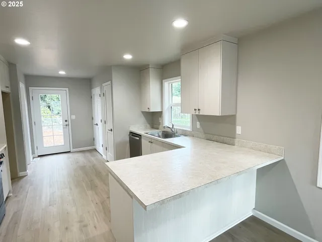 a large kitchen with kitchen island a stove a sink a refrigerator and white cabinets with wooden floor