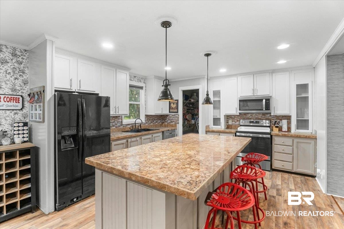 21011 River Road Robertsdale, AL 36567 - Photo 6 of 29 Spacious kitchen featuring a large central island with seating, wood-finish flooring, white cabinetry, integrated stainless steel appliances, and a mosaic tile backsplash