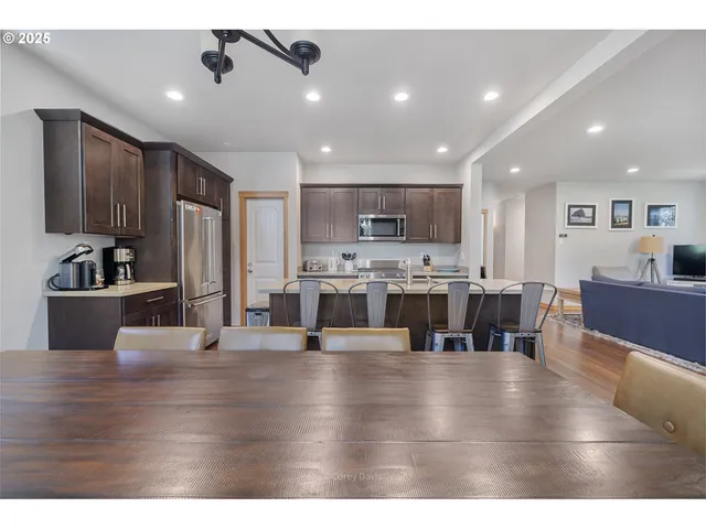a living room with stainless steel appliances furniture wooden floor and a kitchen view