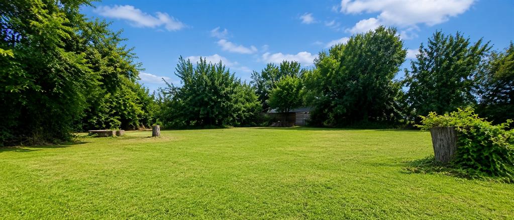504 North Hampton Road DeSoto, TX 75115 - Photo 4 of 11 Expansive grassy lawn surrounded by mature trees, featuring a rustic wooden bench and a wood stump