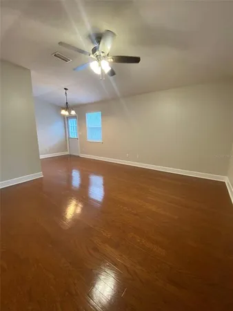 an empty room with wooden floor chandelier fan and windows