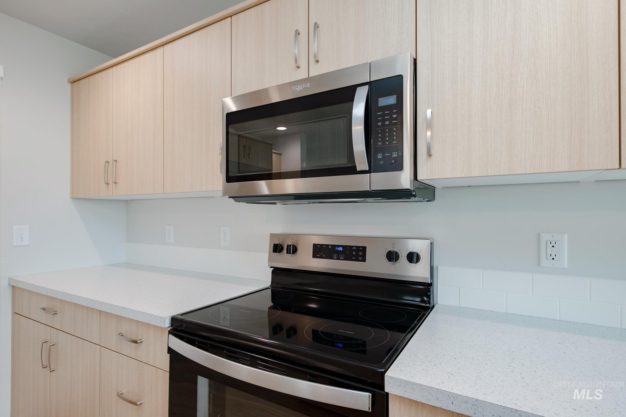 2391 West Fallon Loop Nampa, ID 83651 - Photo 6 of 20 Kitchen featuring light wood-finish cabinetry, stainless steel microwave, electric range, light-toned countertops, and white subway tile backsplash