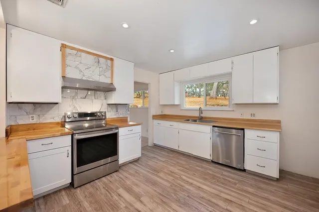 a kitchen with stainless steel appliances granite countertop a stove a sink dishwasher and white cabinets with wooden floor