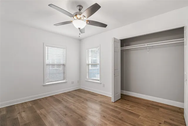 an empty room with wooden floor ceiling fan and windows