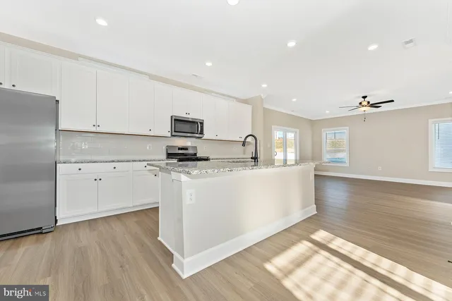 a kitchen with stainless steel appliances granite countertop a stove a sink and white cabinets with wooden floor