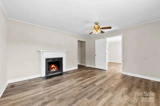 a view of an empty room with wooden floor fireplace and a window