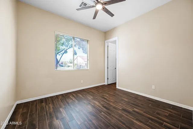 an empty room with wooden floor chandelier fan and windows