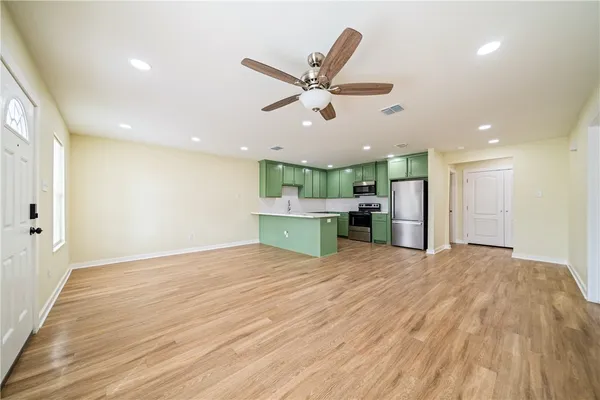a view of an empty room and kitchen with wooden floor and a ceiling fan