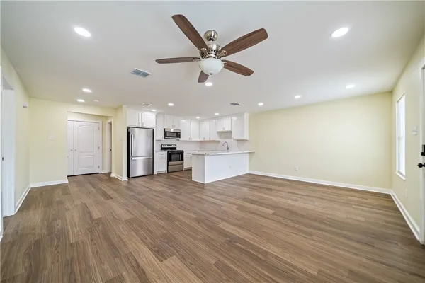 a view of a livingroom with a ceiling fan & kitchen space with wooden floor