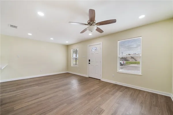an empty room with wooden floor fan and windows