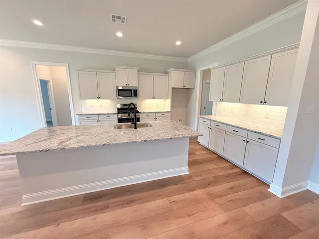 a large kitchen with kitchen island granite countertop a refrigerator a sink and white cabinets