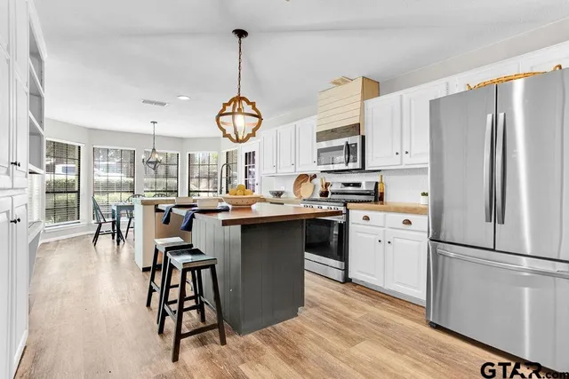 a kitchen with stainless steel appliances granite countertop a refrigerator a stove a sink dishwasher a dining table and chairs with wooden floor