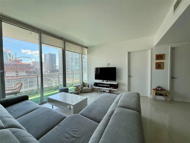 a living room with furniture a flat screen tv and floor to ceiling window