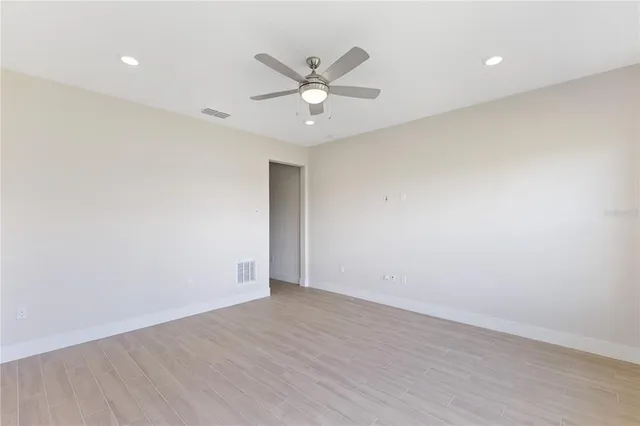 an empty room with wooden floor fan and windows