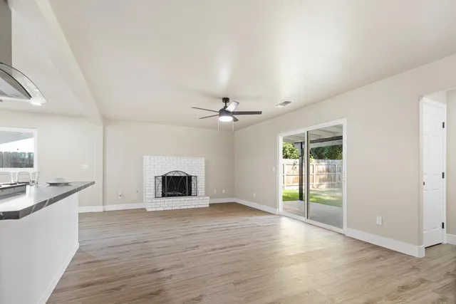 an empty room with chandelier fan and wooden floor