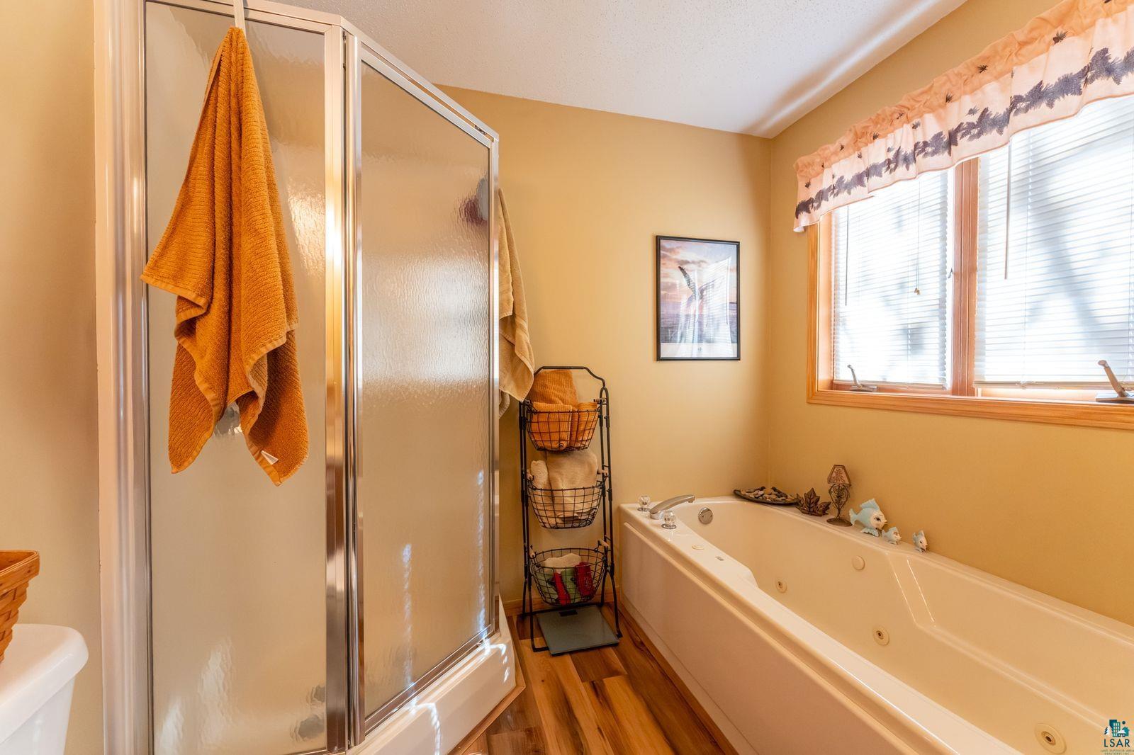 4452 Moccasin Point Road Tower, MN 55790 - Photo 15 of 44 Bathroom featuring a corner shower enclosure, a jetted bathtub, wood-finish flooring, and a large window with blinds