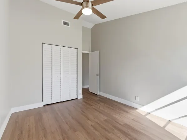an empty room with wooden floor fan and windows
