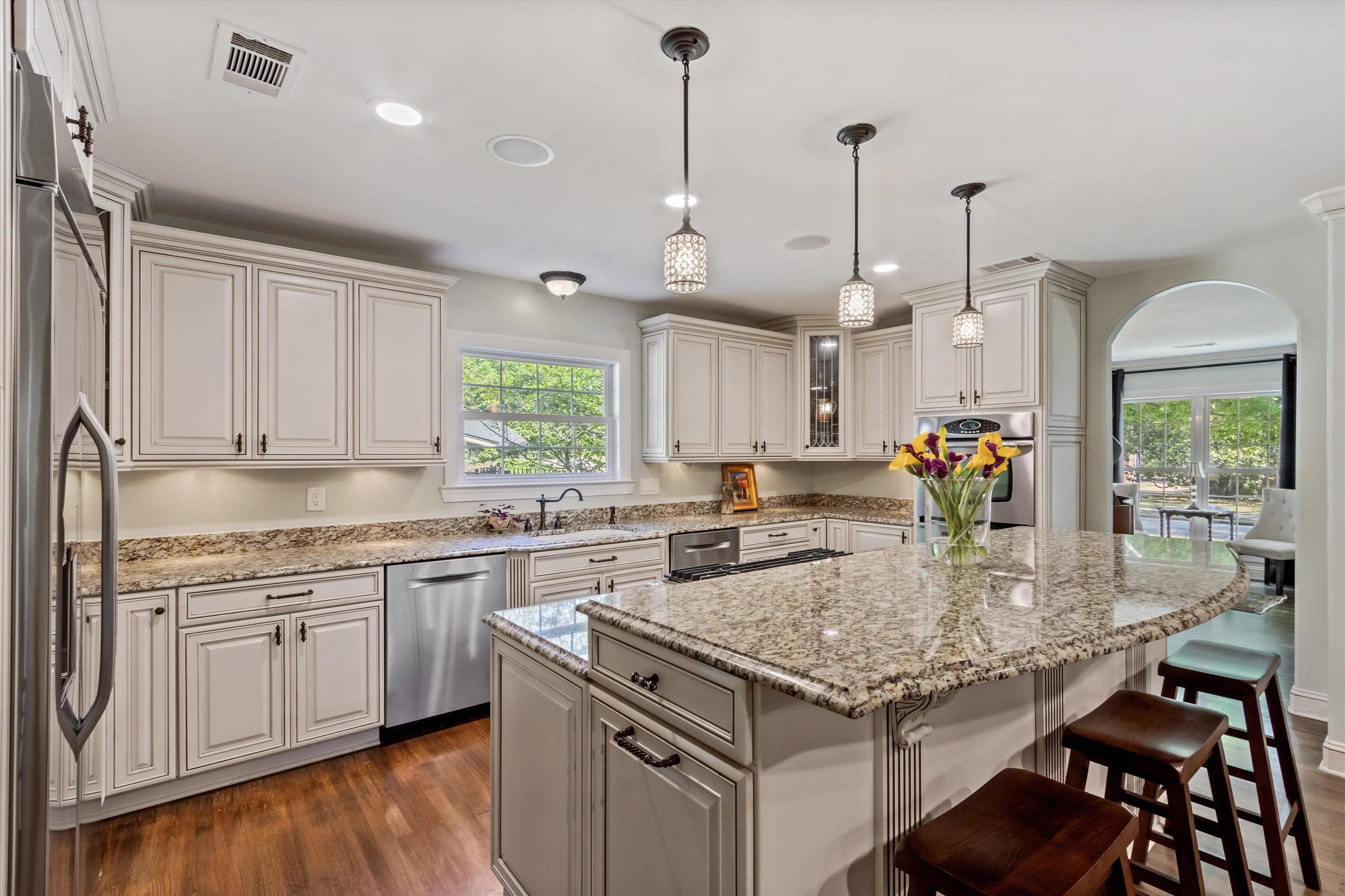 5302 South Angela Road Memphis, TN 38120 - Photo 5 of 40 Spacious kitchen featuring an extended central island with stone countertop, white cabinetry with dark hardware, stainless steel appliances, and rich wood-finish flooring