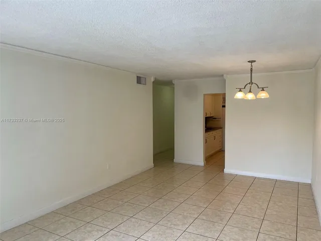 an empty room with chandelier fan and kitchen view