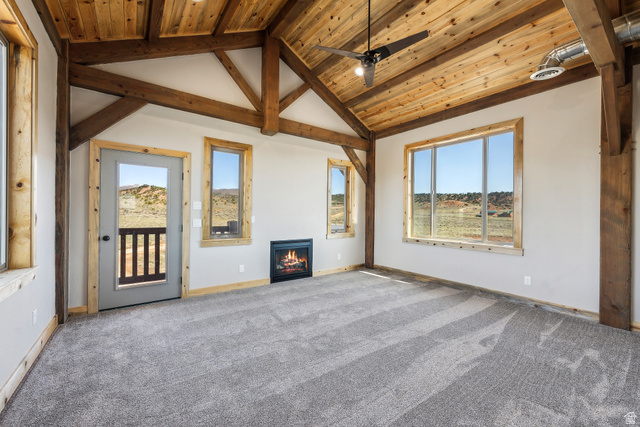 46997 West Thunder Road Fruitland, UT 84027 - Photo 34 of 49 Unfurnished living room featuring a wooden ceiling with exposed beams, carpet floors, a warm lit fireplace, plenty of natural light, and ceiling fan