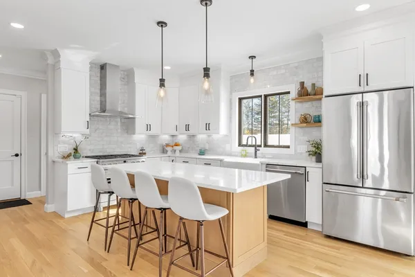 a kitchen with stainless steel appliances granite countertop a sink a stove a refrigerator and white cabinets with wooden floor