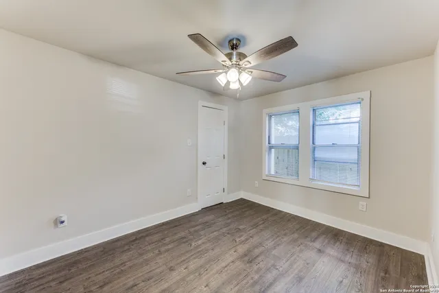 an empty room with wooden floor fan and windows
