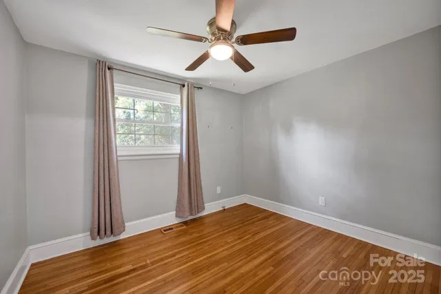 an empty room with wooden floor ceiling fan and windows