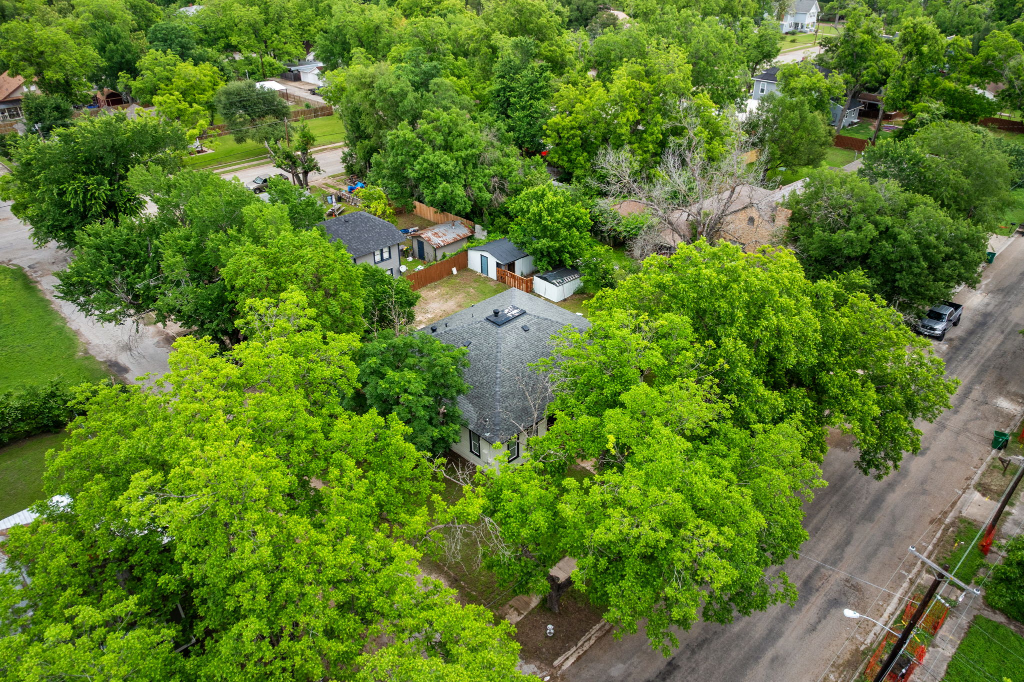 602 East 6th Street Cameron, TX 76520 - Photo 39 of 40 A property nestled among abundant mature trees, featuring a dark shingle roof and light-colored siding