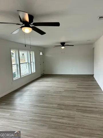an empty room with wooden floor chandelier fan and windows