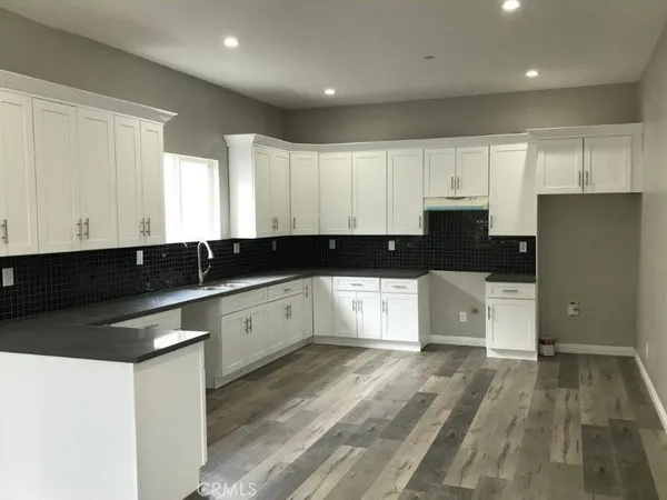 a large white kitchen with granite countertop a stove a sink a refrigerator and white cabinets with wooden floor